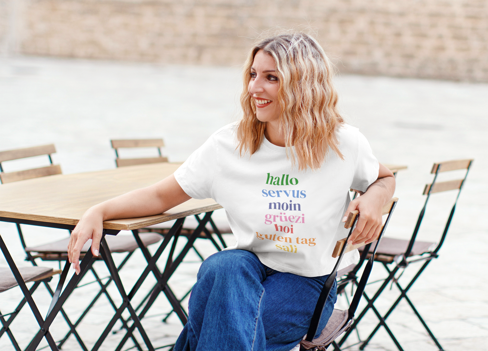 Woman wearing a white t-shirt with colorful text sitting outdoors.